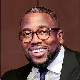 A man with glasses and a beard wearing a suit.